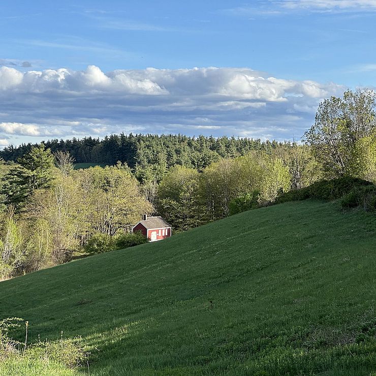 a picture of a field with a small schoolhouse in the background